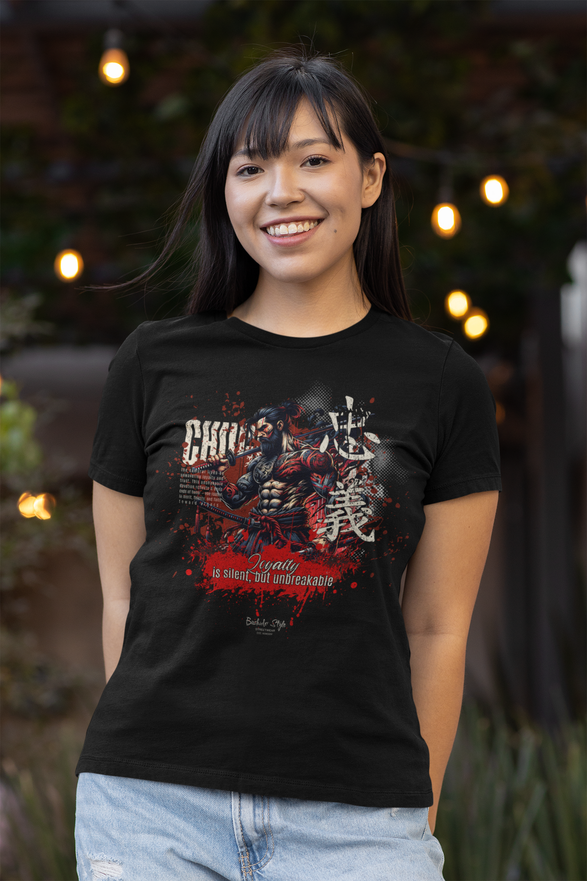 A smiling woman wearing the CHŪGI t-shirt from the 7 Virtues of Bushido series. The shirt features a fierce samurai with red and white ink splashes and the phrase "Loyalty is silent, but unbreakable." Soft outdoor lights glow in the background.