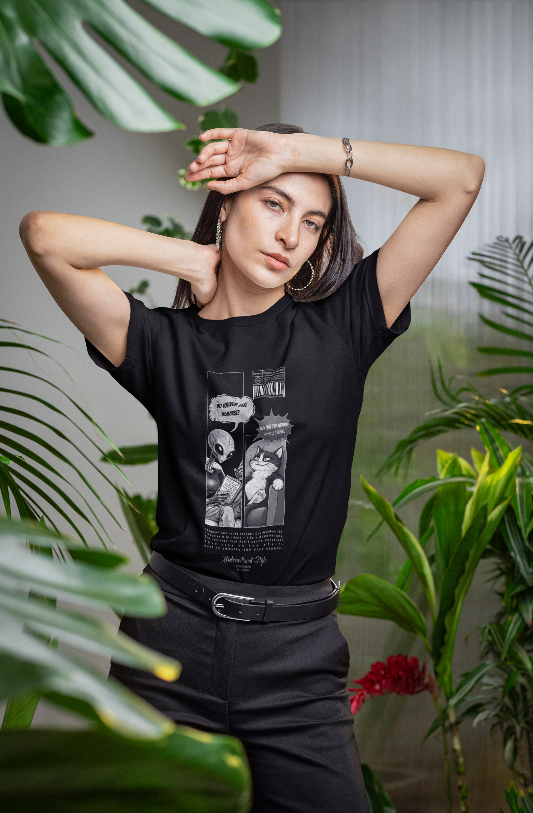 Woman model posing with a relaxed hand-over-forehead gesture in a bright, plant-filled indoor setting, wearing the black "FEEL REMORSE?" graphic tee. The design features a black-and-white comic panel: an alien therapist asks, “Do you ever feel remorse?” — the cat responds, “No. But I’ve heard it’s a thing.” The t-shirt merges sarcastic humor with clean visual storytelling. Design is centered on the chest with barcode and microtext details.