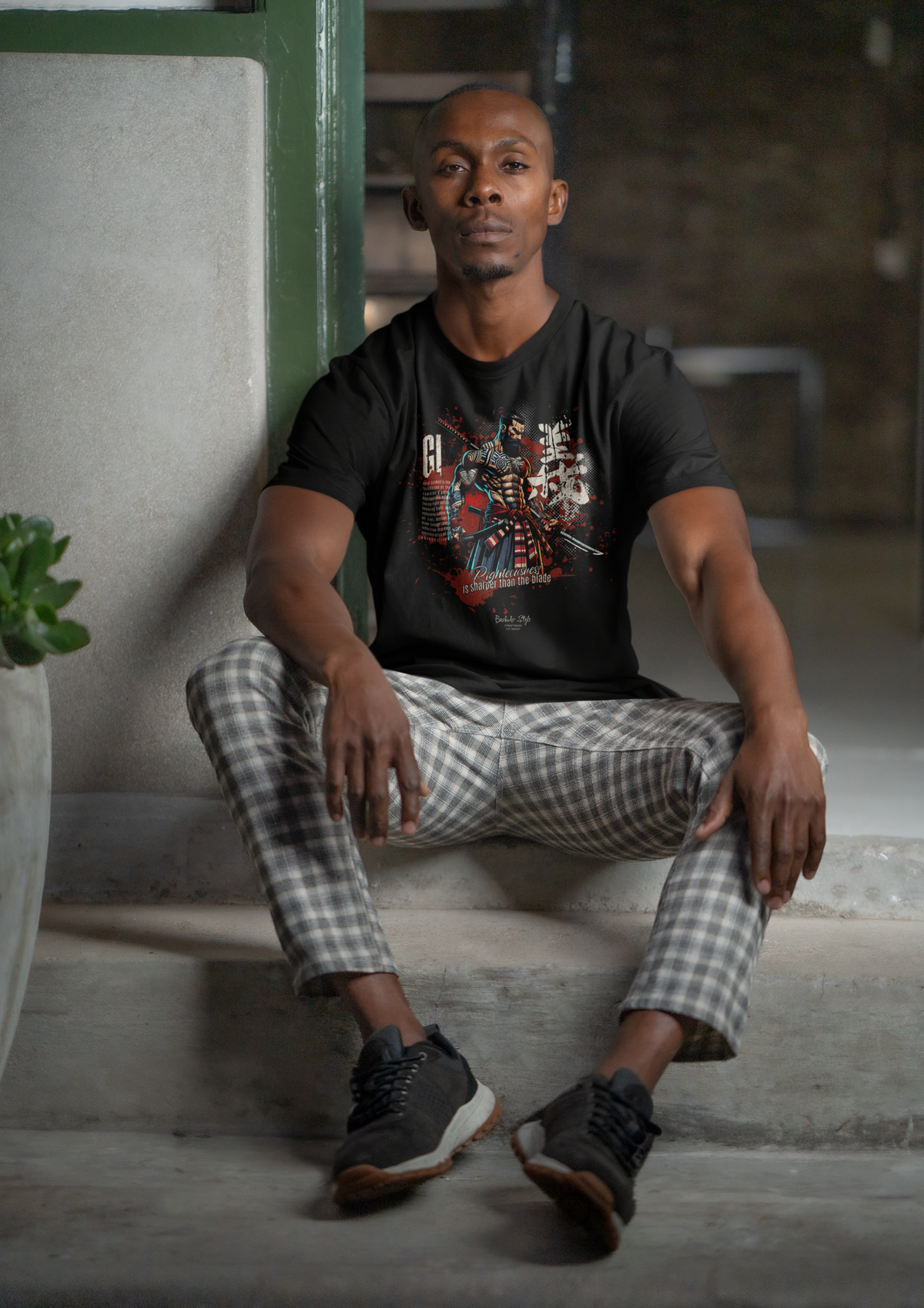 A stylish male model sits casually on stairs, wearing the GI t-shirt. His pose and the design’s strong red tones reflect inner strength and conviction.