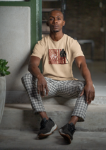 “No Retreat No Surrender” sanddune tee by KRASSWERK – worn by male model sitting on concrete steps in modern indoor setting, calm pose and checkered pants highlight relaxed confidence