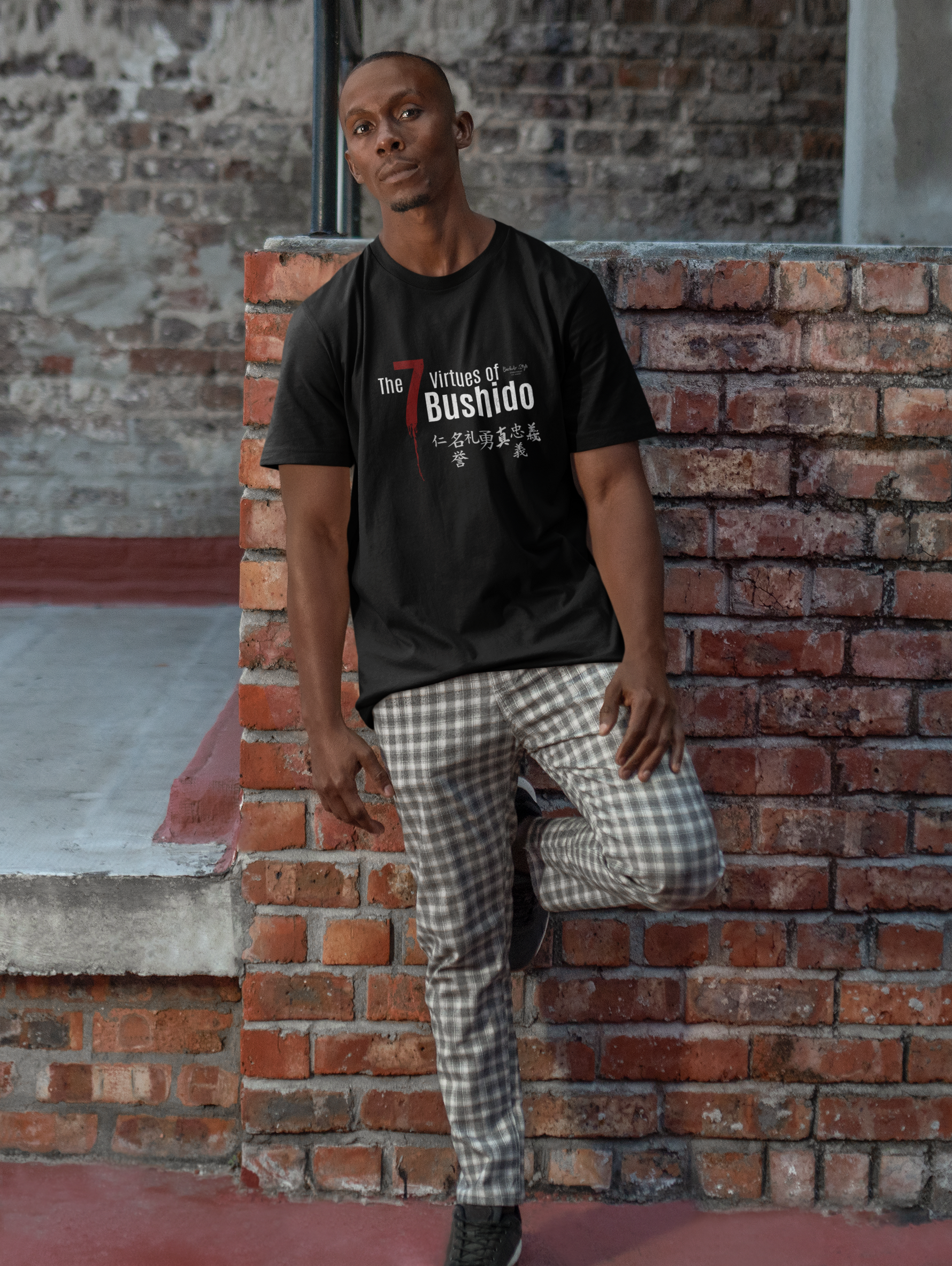 The 7 Virtues of Bushido black tee by KRASSWERK – worn by male model in outdoor brick backdrop, calm upright pose reflecting quiet strength