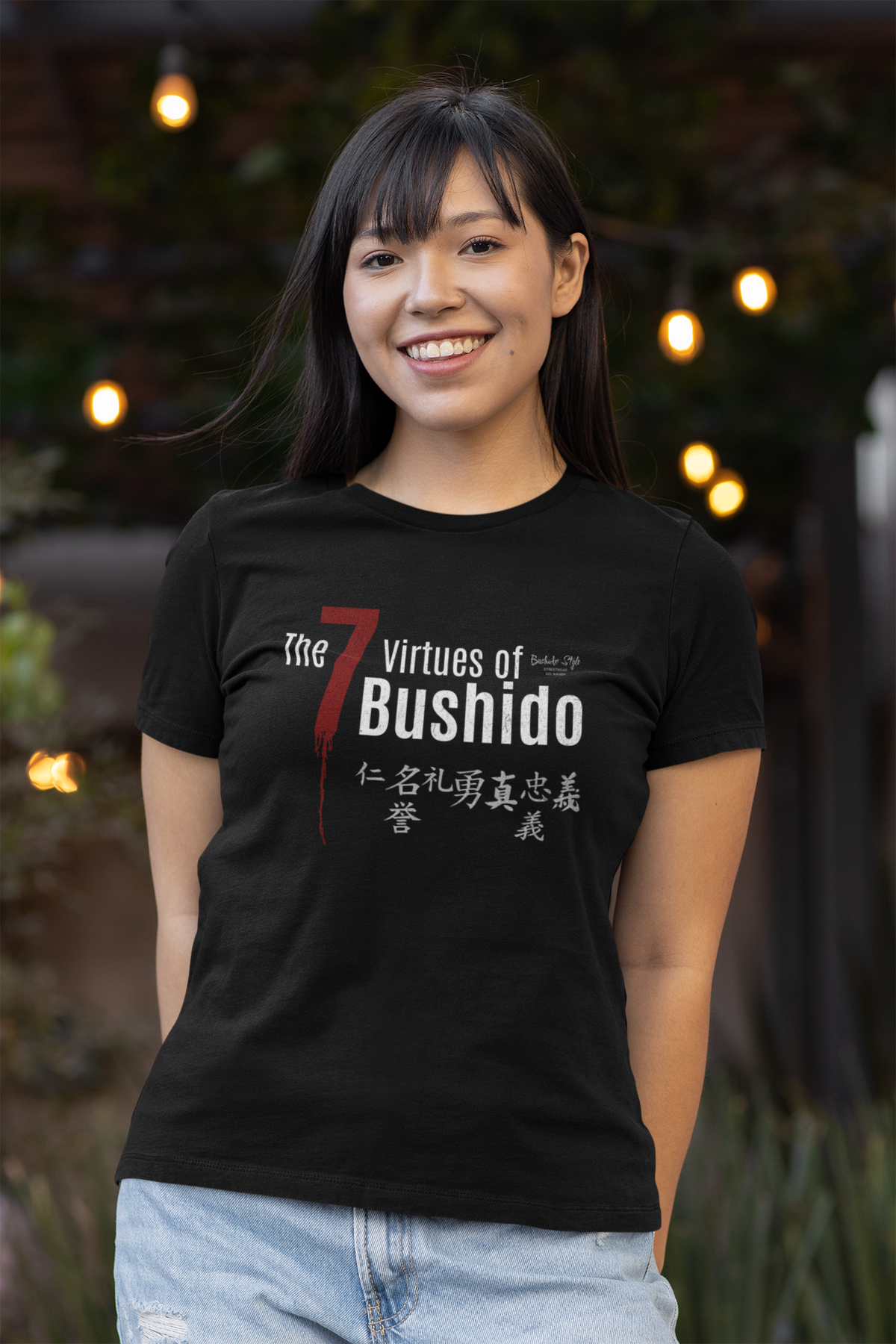 The 7 Virtues of Bushido black tee by KRASSWERK – worn by female model in evening outdoor setting with warm lights, balanced smile and soft contrast