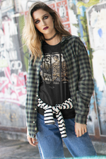 “BADASS” black tee by KRASSWERK – worn by female model in grunge street backdrop, layered with flannel shirt and striped sweater, samurai warrior graphic on full display