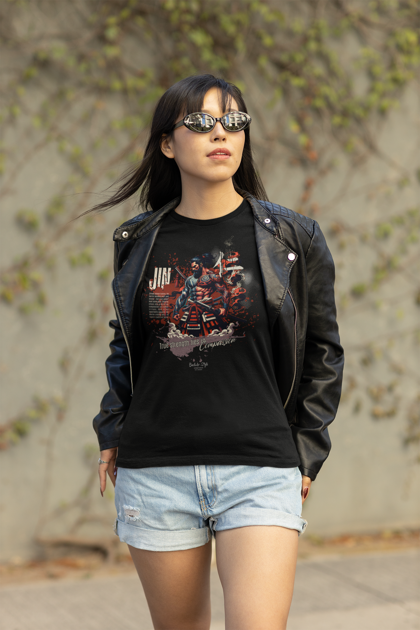 “JIN” black tee by KRASSWERK – worn by woman in leather jacket and sunglasses, urban street backdrop, showcasing warrior artwork and compassion message
