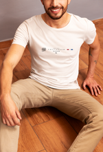 Man wearing a white t-shirt with branding sitting on a wooden floor.