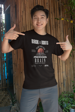 Male model smiling and pointing at his black “Back to the Roots” t-shirt featuring a stylized brain. Natural outdoor setting with bamboo background and casual vibe.
