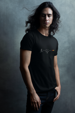 A young man with long, flowing hair poses in a black “BARCELONA” Krasswerk t-shirt against a moody, textured gray background. His eyes are gently closed, head slightly turned, and his hand rests casually in his pocket, creating a poetic, introspective atmosphere. The shirt features a minimalist city name and flag design on the chest, standing out against the dark fabric with subtle contrast.
