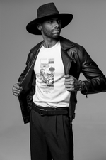 A confident male model wearing a wide-brim black hat and leather jacket opens his jacket to show a white t-shirt with a comic-style black-and-white design. The print features an alien therapist asking “Can you try being nicer?” and a sarcastic cat replying “Can you try being useful?” The photo is shot in a studio with a plain background and presented in black and white, highlighting the shirt’s bold artwork and the model’s strong posture.