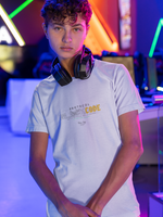 Indoor lifestyle shot of a young man with curly hair and headphones around his neck, wearing a white “PROTOCOL BLACKCODE” t-shirt. The design displays smokey “BLACK” text and bold yellow “CODE” with the phrase “NOT IN THE SYSTEM. NOT IN CONTROL.” The setting is a neon-lit gaming lounge with futuristic light patterns in the background.