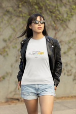 Outdoor lifestyle shot of a woman in sunglasses and a black leather jacket, walking confidently in daylight while wearing a white “PROTOCOL BLACKCODE” t-shirt. The design features a smokey “BLACK” text and yellow “CODE” with the phrase “NOT IN THE SYSTEM. NOT IN CONTROL.” Background includes a blurred concrete wall with scattered ivy.