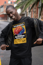 A cheerful male model standing on an urban street pulls open his jacket to reveal a bold black t-shirt featuring a vibrant warning label: “BRAIN ACTIVITY DETECTED.” The colorful brain graphic and distressed yellow frame pop with rebellious energy — the perfect mix of humor and street-smart style.