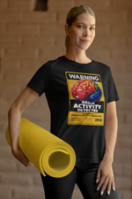 A sporty female model holding a rolled yellow yoga mat stands in a relaxed pose, wearing a black graphic t-shirt with a bold warning label: “WARNING – BRAIN ACTIVITY DETECTED.” The colorful 3D brain artwork contrasts sharply against the black tee, delivering a clever mix of humor and intellect.