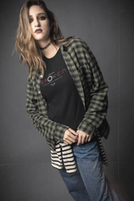 Person wearing a plaid shirt over a black t-shirt with visible branding on a gray background