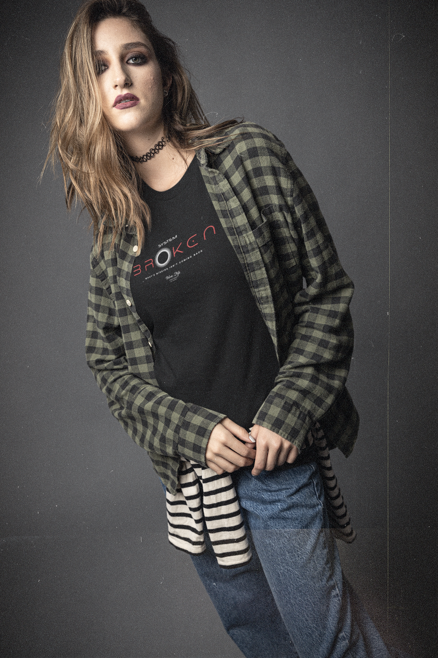 Person wearing a plaid shirt over a black t-shirt with visible branding on a gray background