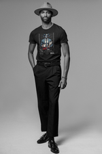 A confident male model in a wide-brim hat and leather jacket poses in-studio wearing the “CAPRICORN” graphic tee in black. The design features a suit-wearing goat-horned character holding a mugshot board. Clean monochrome setting adds contrast to the shirt’s colors.