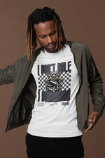 Man in a bomber jacket and corduroy pants pointing toward his white t-shirt, which features a commanding cat on a throne with checkered background and the phrase “I DON’T RULE. I COMMAND.” on a warm brown backdrop.