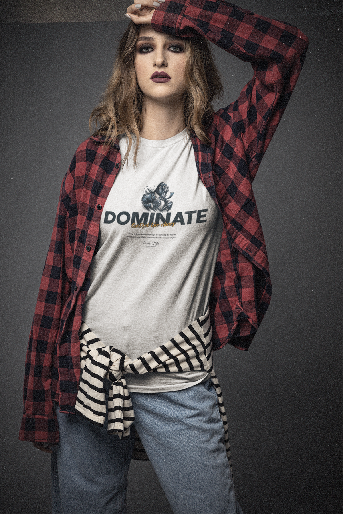Confident woman wearing the DOMINATE t-shirt with layered streetwear — bold makeup, flannel shirt, and attitude. The mechanical fist on the tee contrasts with her casual yet commanding stance. A quiet kind of power that doesn’t ask.