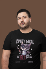 Confident man in a black “EVERY MEAL IS MY MEAL” t-shirt, featuring a mischievous cat graphic with sunglasses and a fork. Posed against a plain brown background, emphasizing the bold design and laid-back expression.