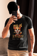 Man in a black cap and beige pants takes a selfie while wearing a black t-shirt that features a wide-eyed cartoon kitten holding a bowl with the phrase “FEED ME OR FACE THE CONSEQUENCES.”
