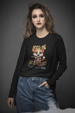 Woman with bold makeup and casual streetwear poses confidently in a studio while wearing a black t-shirt that says “FEED ME OR FACE THE CONSEQUENCES” featuring a cute but demanding cartoon kitten holding a food bowl.