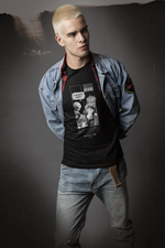 Male model with bleached hair wearing a layered denim jacket and vintage jeans, posing against a grungy studio backdrop. The black "FEEL REMORSE?" comic-style t-shirt takes center stage with a bold monochrome design: an alien holds notes while asking, “Do you ever feel remorse?” — the cat leans back, unfazed, replying, “No. But I’ve heard it’s a thing.” The shirt blends sarcastic narrative with sci-fi attitude, capturing the brand’s unapologetic edge.