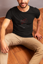 Male model sitting casually on a wooden floor, smiling confidently while wearing the FERAL t-shirt in black — the bold claw-scar logo and "Too Wild to Follow" text stand out in the relaxed indoor setting.