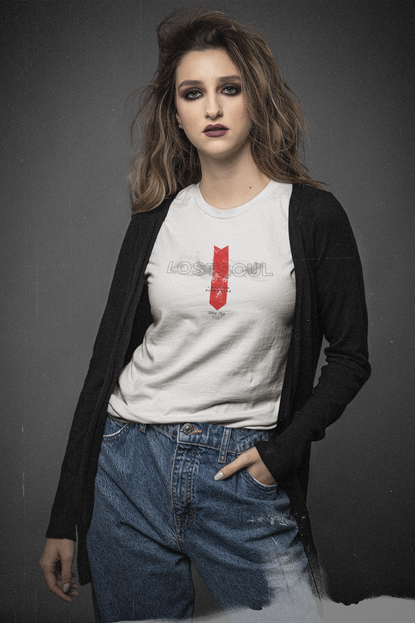 Female model in denim jeans and a black cardigan, wearing the “LOSTSOUL” white t-shirt. The design features transparent smoky text and a bold red downward arrow. Shot against a dark grey background with a gritty, cinematic tone.
