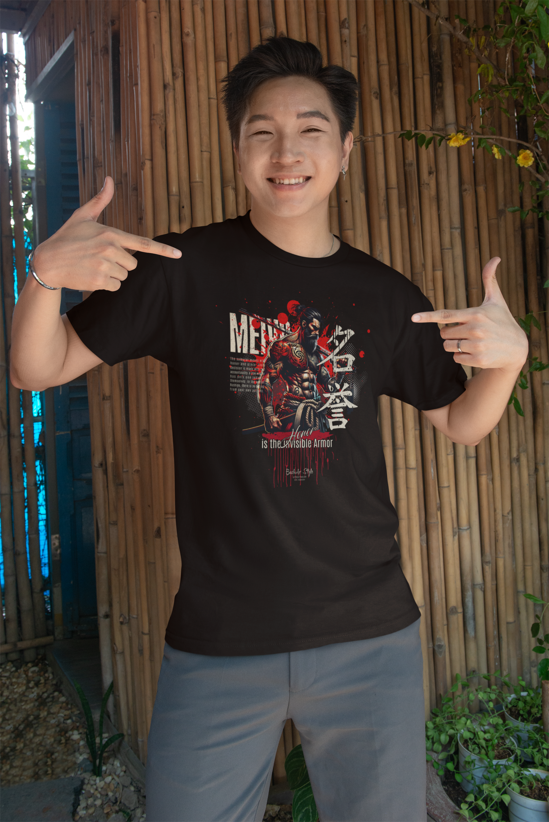 “MEIYO” black t-shirt by KRASSWERK – lifestyle photo of smiling man in casual shorts, pointing proudly at honor-themed samurai design in a tropical outdoor setting