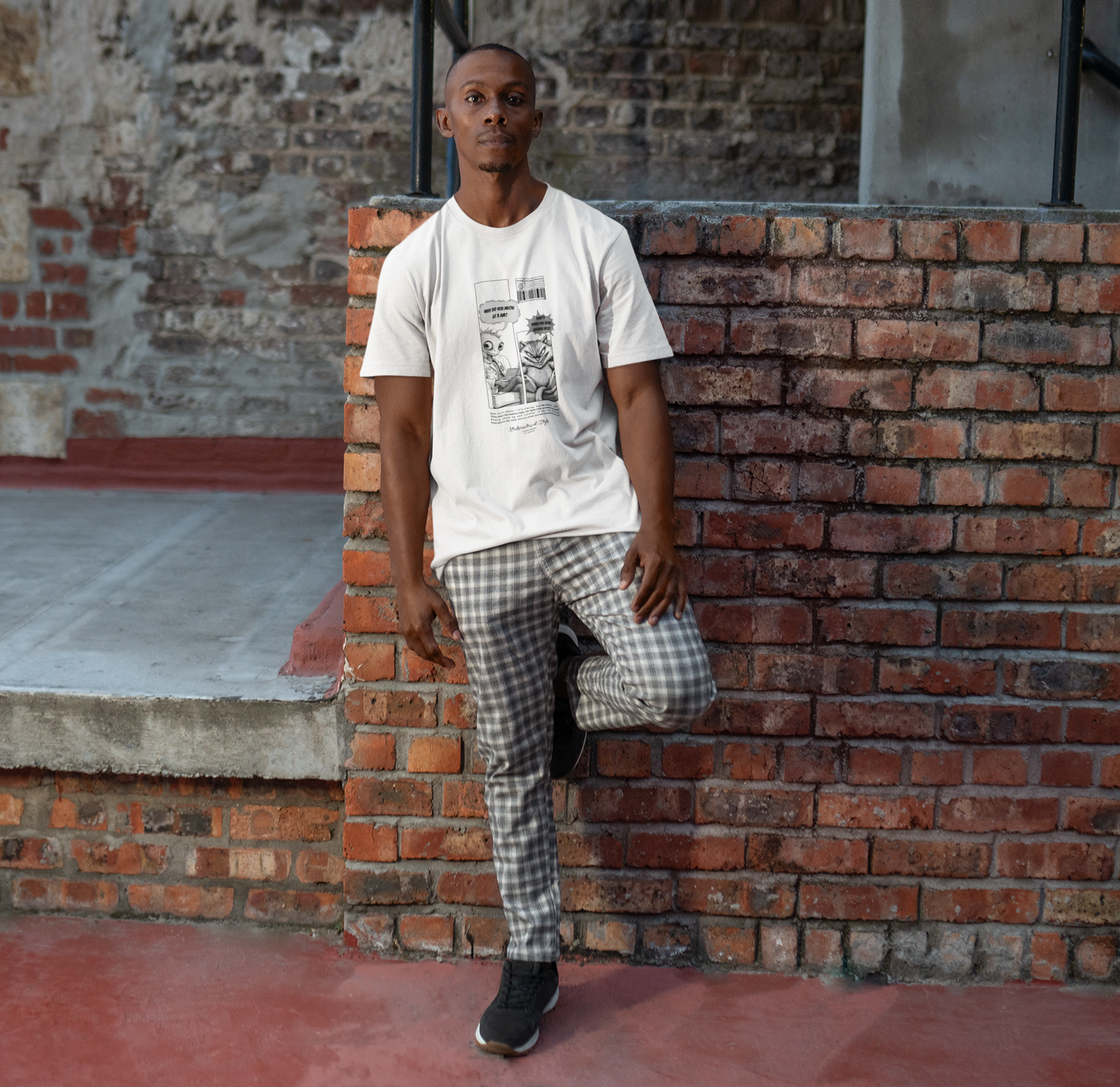 A man leans casually against a brick wall in an urban alleyway, wearing a white t-shirt with a comic-style graphic. The design features a surreal alien asking, “Why do you meow at 3 A.M.?” and a smug-looking cat answering, “That’s when the void listens best.” The scene blends street fashion with dry humor, and the model pairs the tee with checkered pants and sneakers for a laid-back city look.