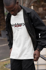 Urban streetwear photo of a man in black windbreaker looking down at his white “NO MERCY – Just Results” t-shirt; bold black and red typography stands out in a casual outdoor scene.