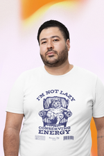 Man with short hair and beard stands confidently against a pastel orange gradient background, wearing a white “I’M NOT LAZY — I’m Just Conserving Energy” t-shirt with a lounging cat in a vintage chair.