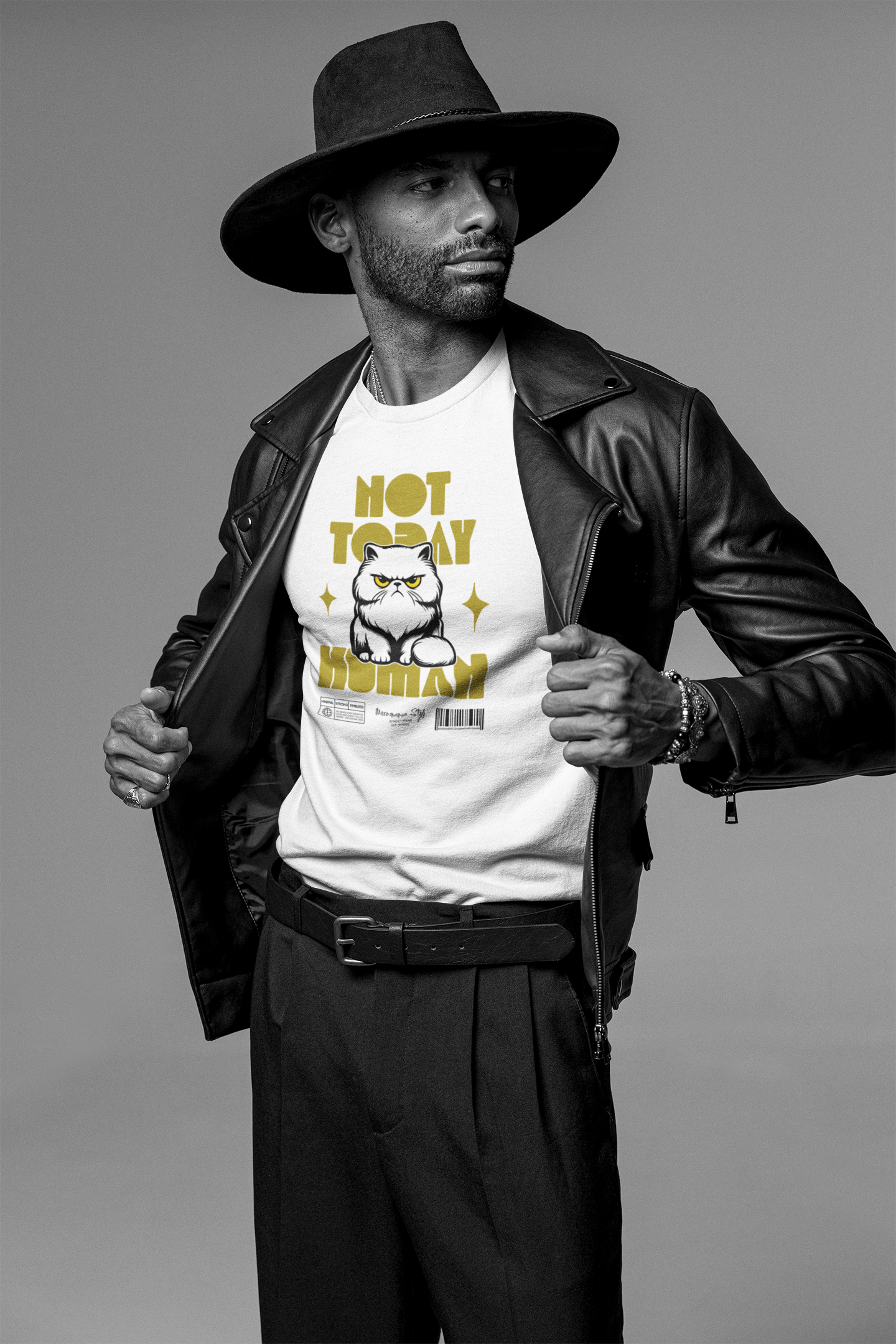 A confident man in a wide-brimmed hat and leather jacket opens his coat to reveal a white t-shirt featuring an angry cartoon cat and the bold text 'NOT TODAY HUMAN' in yellow. The grayscale background enhances the bold yellow print, while the model’s stylish look adds contrast and edge to the humorous design.