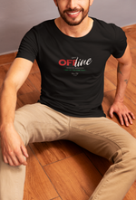 A man sits casually on a wooden floor wearing a black “UNIT OFFLINE” T-shirt with glitch-style red and white text. He smiles slightly, with beige pants contrasting the modern streetwear look.