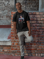 A man leans back against a red brick wall with one foot raised, looking calmly at the camera. He wears a black t-shirt showcasing the “PISCES – Lost In Dreams” mugshot design, featuring a pensive man in striped pajamas holding a placard in front of a police lineup backdrop.
