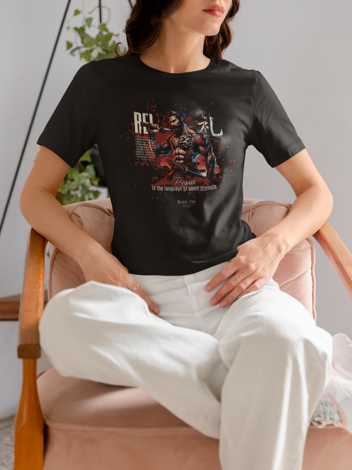“REI” black t-shirt by KRASSWERK – lifestyle photo of woman seated in soft-lit interior, wearing Bushido-inspired respect-themed graphic tee with red and black samurai design