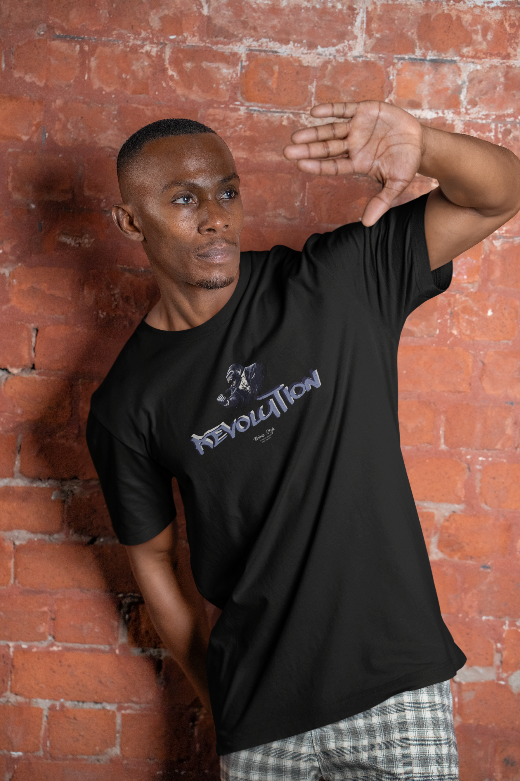 REVOLUTION black tee by KRASSWERK – worn by male model in urban lifestyle setting, strong pose against brick wall backdrop
