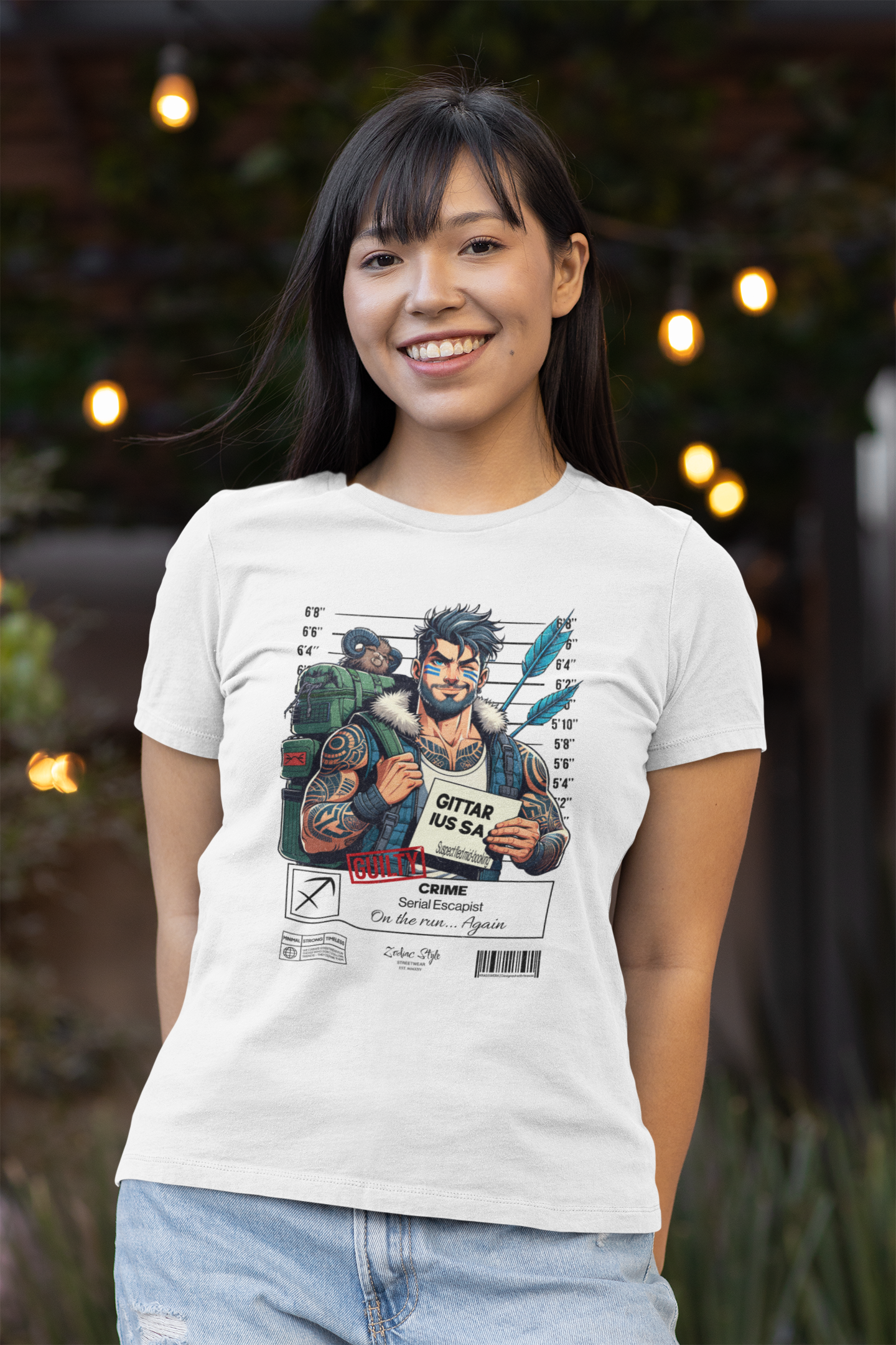 White t-shirt worn by a smiling woman standing outdoors in soft evening lighting. She wears the Sagittarius “Serial Escapist” design, showing a bearded traveler holding a guilty sign, arrows on his back, and a raccoon on his backpack. Background lights add a cozy atmosphere.