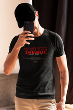 Man in beige pants and black cap taking a mirror selfie, wearing the black SAVAGE t-shirt with red “Wired Different” print — casual, confident, and unfiltered street energy.