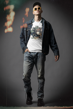 A confident man standing with relaxed posture in a studio setting, wearing THE ARCHER t-shirt design featuring a crouched archer mid-draw and the slogan “Strike True. Strike Silent.” Moody lighting with film burn effects highlights the vintage warrior aesthetic.