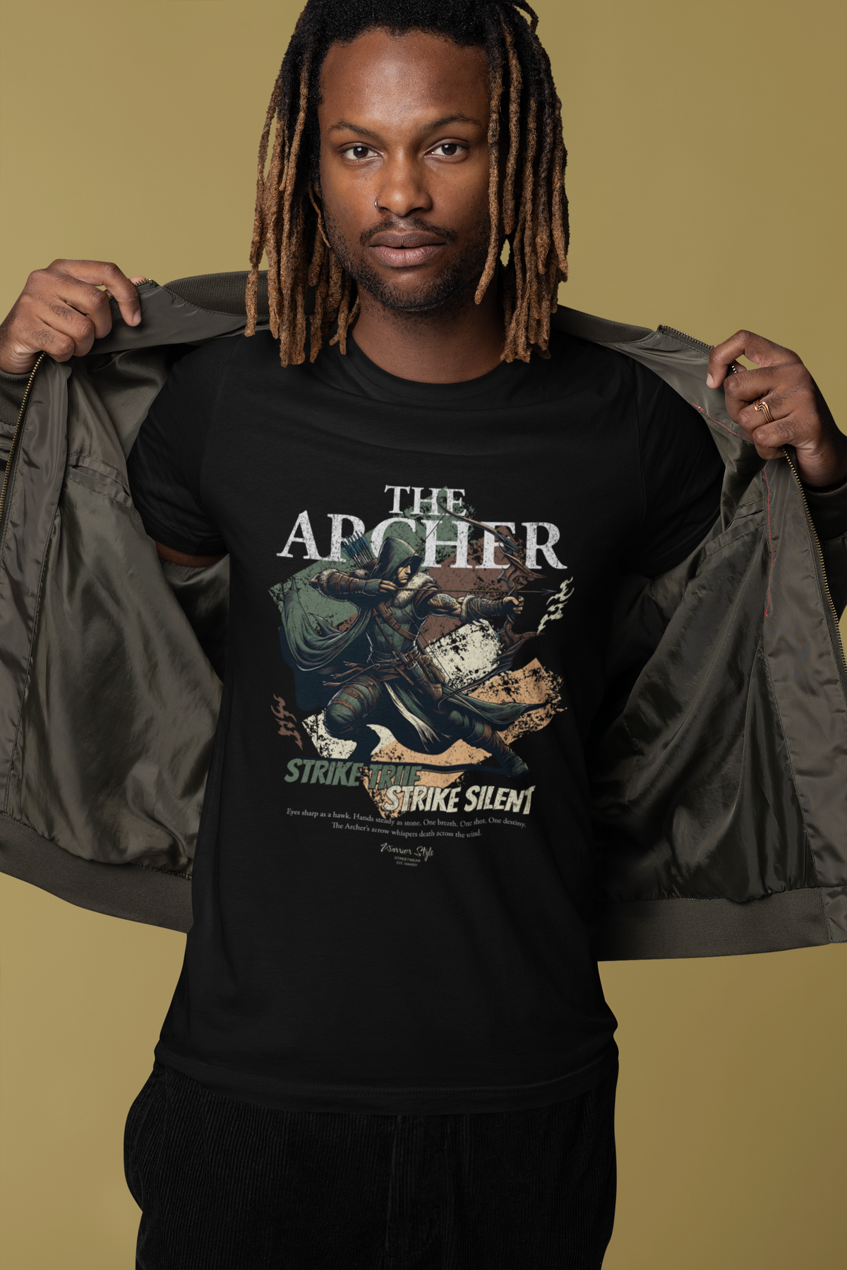 A confident man smiling in a studio setting, opening his jacket to reveal THE ARCHER t-shirt design featuring a crouched archer mid-draw and the slogan “Strike True. Strike Silent.” A warm beige background adds contrast to the dark tee and highlights the character’s focused stance.