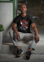 A man seated on concrete stairs in a dimly lit space, wearing the KRASSWERK 'THE BARBARIAN' black t-shirt. His expression is calm but strong, enhancing the bold, primal vibe of the warrior-themed graphic.