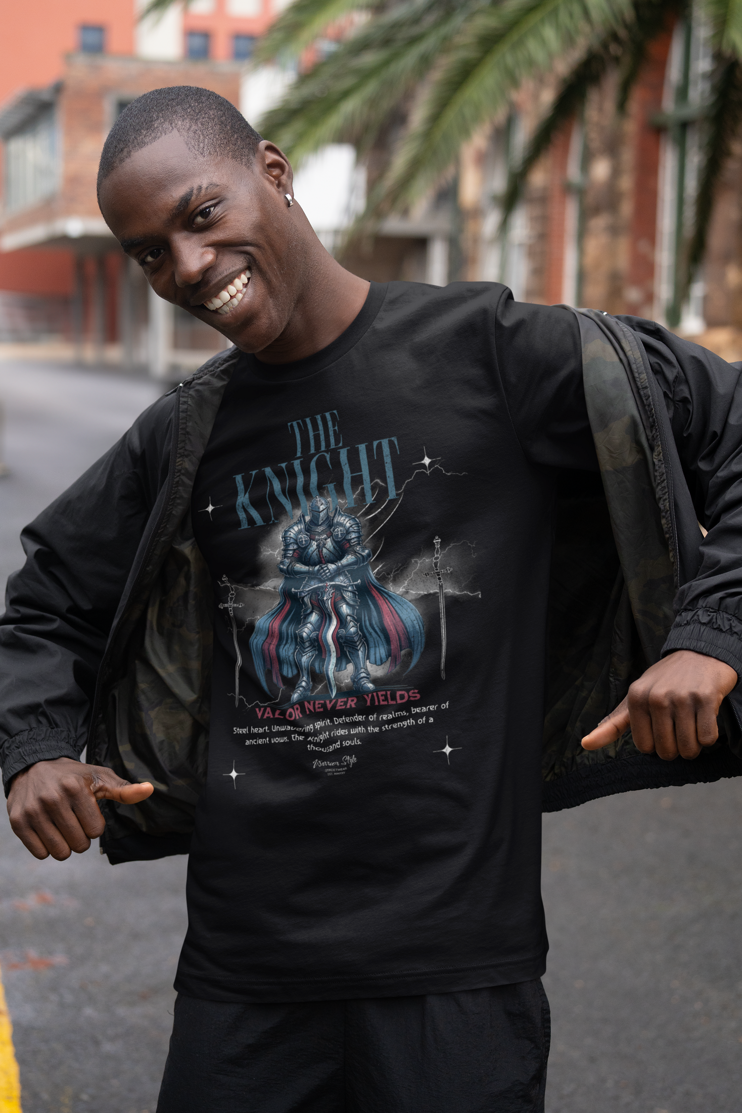 A confident man smiling in an urban setting, opening his jacket to reveal THE KNIGHT t-shirt design featuring a blue-armored warrior and the slogan “Valor Never Yields”.