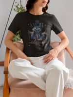 A woman sitting calmly in a velvet chair, wearing THE KNIGHT t-shirt featuring a blue-armored figure and the phrase “Valor Never Yields”, styled with a relaxed yet strong presence.