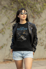 Female model walking outdoors in sunglasses and leather jacket, wearing the black THE NINJA t-shirt with a dynamic mid-kick ninja illustration and the phrase “Silent. Swift. Deadly.”