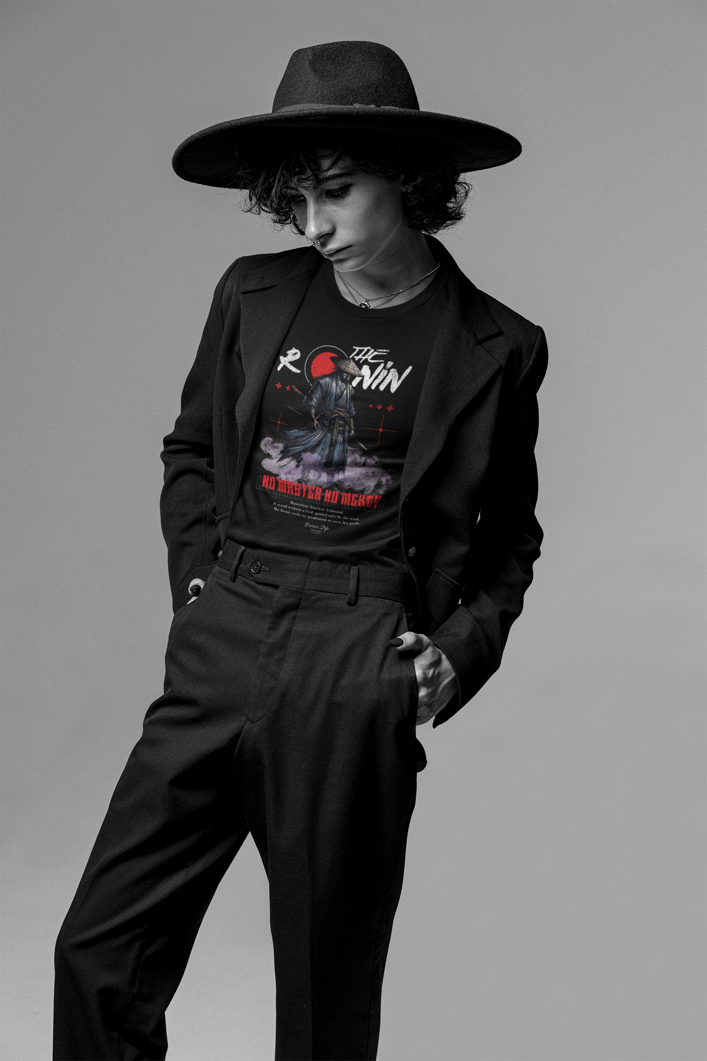 Model wears The Ronin t-shirt under a wide-brim hat and blazer — calm pose reflects the shirt’s lone warrior theme.