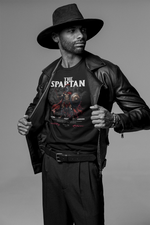 A bold male model in a black leather jacket and wide-brim hat reveals THE SPARTAN t-shirt. The design features a warrior with shield and spear, captioned with “Stand. Fight. Endure.” in red and white.