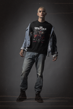 A bold male model in denim and boots stands strong in THE SPARTAN t-shirt. The design features a battle-worn Spartan warrior with the words “Stand. Fight. Endure.” beneath him.