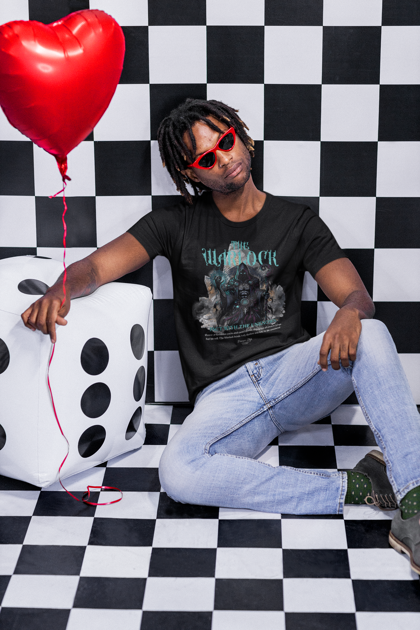 A man in red sunglasses sits casually against a giant dice, wearing THE WARLOCK t-shirt in black — a mystical design radiating arcane energy and otherworldly presence.