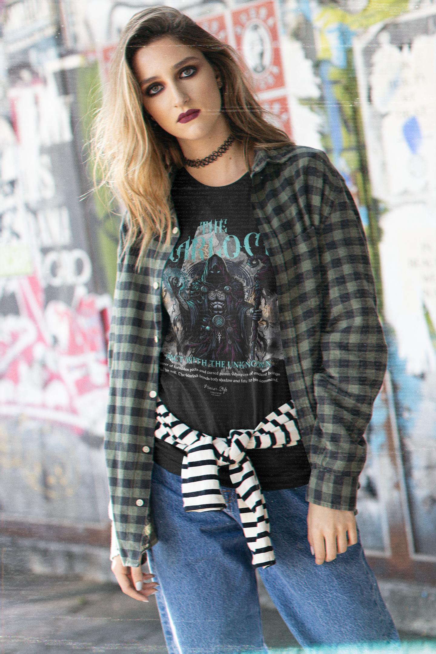 A young woman with smoky eye makeup stands against a graffiti wall, wearing THE WARLOCK t-shirt in black — channelling dark mystique and unspoken power.