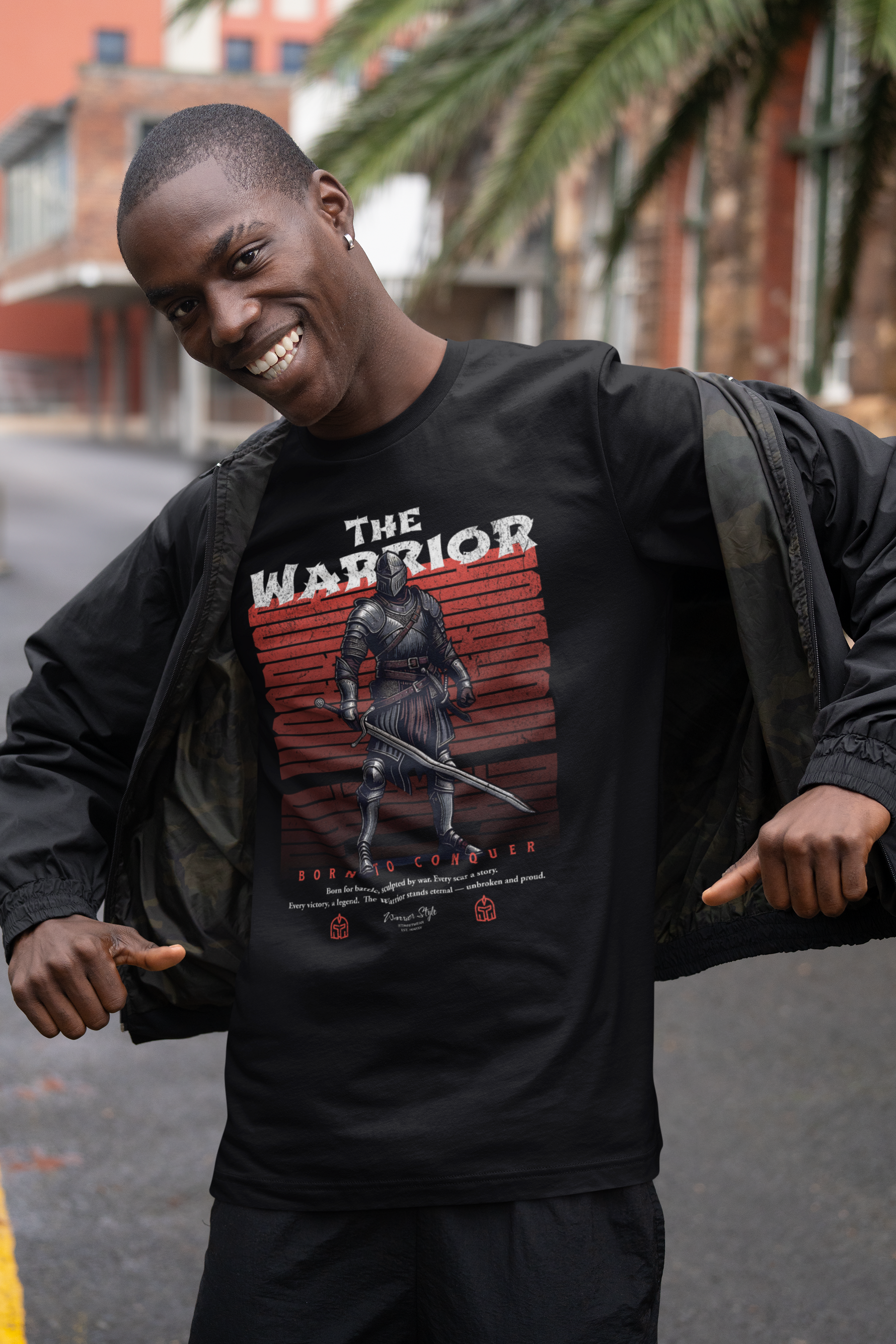 Man smiling in urban street while opening jacket to reveal THE WARRIOR t-shirt — showcasing the bold knight design with 'Born to Conquer' slogan front and center.